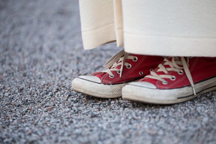 Bilder visar en fötterna på en konfirmand med alba och röda converse skor.